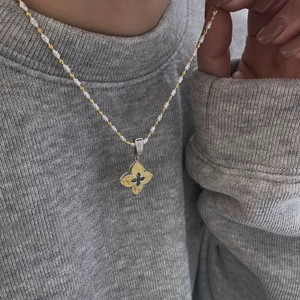 Détail du collier de perles bicolores avec pendentif floral texturé sur le mannequin