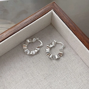 Detail view of S925 sterling silver hoop earrings with unique pleated texture on linen