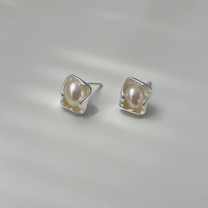 Close-up of irregular silver wave frame earring with white teardrop pearl detail