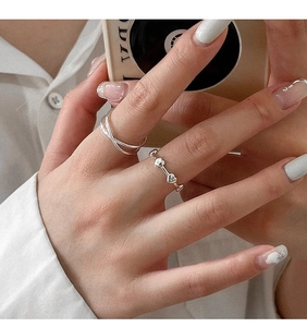 Detail von gestapeltem S925 Silber-Herzring und Kreuzband am Finger des Models