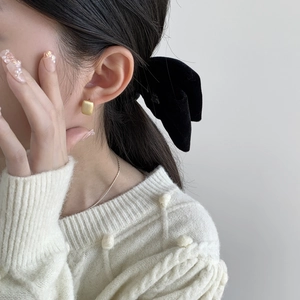 Détail de boucles d'oreilles carrées dorées mates portées par un modèle élégant