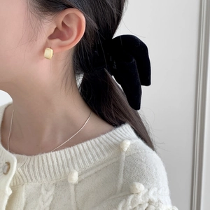 Gros plan sur des boucles d'oreilles carrées dorées mates et un collier en argent