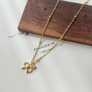 Close-up of golden bow-shaped pendant with cubic zirconia on a beaded chain necklace