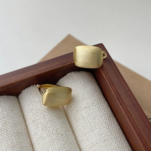 Détail de boucles d'oreilles carrées dorées avec finition brossée mate en boîte bois