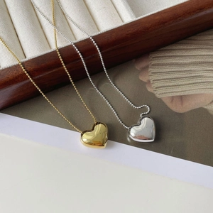 Détail de pendentifs en forme de cœur argent et or sur des chaînes à billes sur plateau