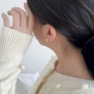Gros plan d'une boucle d'oreille anneau dorée mate sur un modèle en pull en maille blanc