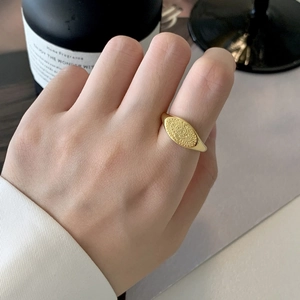 Détail macro d'une bague chevalière ovale dorée avec totem soleil sur un doigt féminin