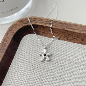 Collier fleur en argent avec pierre noire et texture martelée sur plateau de luxe