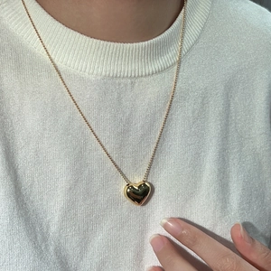 Détail d'un pendentif cœur doré bombé sur une chaîne à billes portée sur un tricot blanc