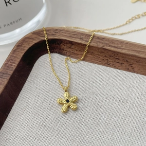 Détail du collier à pendentif fleur dorée avec texture martelée et pierre noire centrale