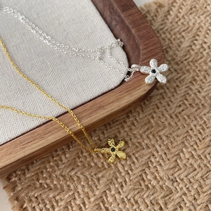 Détails de colliers à fleurs en or et argent avec texture martelée et pierres noires centrales