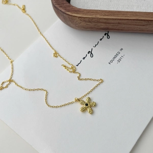 Détail du collier fleur avec pierre noire et texture martelée sur chaîne dorée
