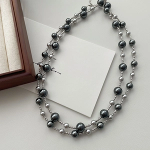 Double-layer gradient grey faux pearl necklace with metallic luster on white leather surface