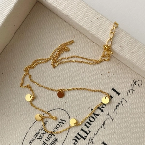 Detail of a minimalist gold 925 silver necklace with round disc charms on a fabric background