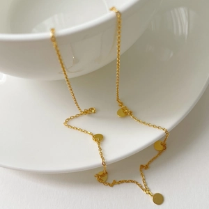 Detail of a minimalist gold pendant necklace draped over a white ceramic coffee cup