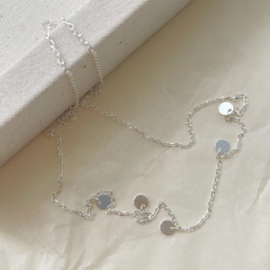 Detailed close-up of a minimalist silver necklace with five polished circular pendants on a white fabric