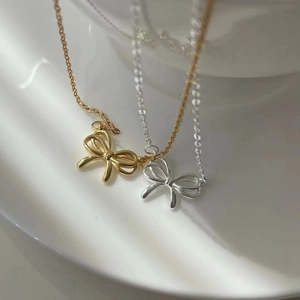 Stereo hollow ribbon bow necklaces in gold and silver finish on white ceramic