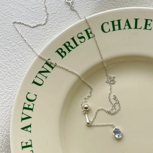 Detail of S925 silver necklace with blue teardrop zircon pendant on elegant ceramic plate