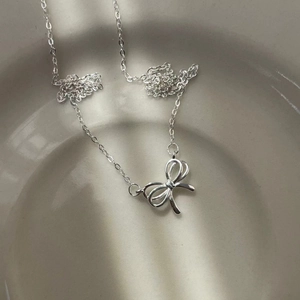 Detailed close-up of a 925 sterling silver hollow bow pendant necklace in a ceramic dish