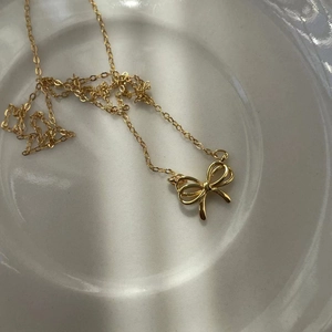 Detailed macro shot of a golden bow pendant necklace resting on a white ceramic plate