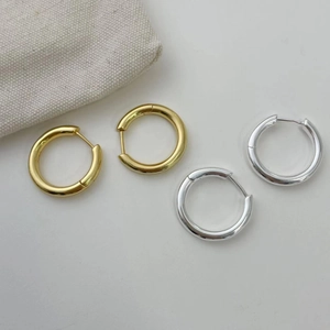 Créoles polies en or et argent avec fermoir à cliquet sur un fond de couleur neutre