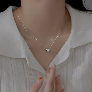 Close-up of polished 3D heart pendant on fine silver box chain worn by a model