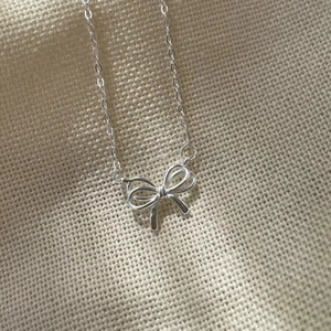 Close-up of 925 sterling silver hollow bow pendant necklace on textured fabric