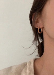 Gros plan d'un mannequin portant des créoles dorées minimalistes et des boucles d'oreilles