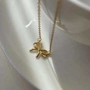 Close-up of golden hollow bow pendant necklace draped on white curved porcelain