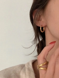 Gros plan de boucles d'oreilles créoles dorées et d'une bague à plusieurs rangs