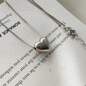 Macro detail of a 925 silver heart pendant necklace with polished mirror finish on white paper