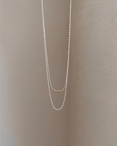 Dettaglio di una collana minimalista a due strati con pendente a chicco d'oro su catena argento