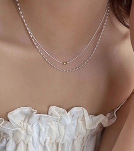 Dettaglio della collana a strati in argento S925 con perla cilindrica dorata sulla clavicola