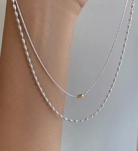 Dettaglio di collane sovrapposte in argento S925 con perla dorata e catena a chicchi