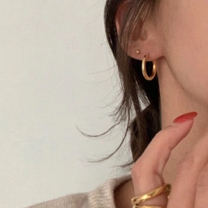 Créoles dorées minimalistes et bague torsadée double couche portées par le modèle