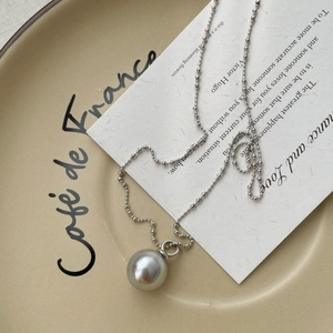 Close-up of a silver grey pearl pendant on a beaded chain over elegant card and tray