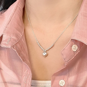 Detail of silver heart necklace with olive bead chain on a pink shirt collar