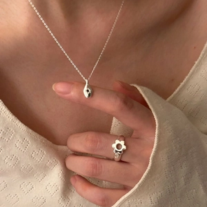 Detail of silver necklace with teardrop pendant and elegant hollow floral ring on model