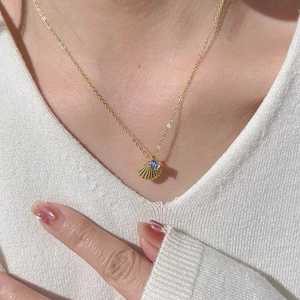 Close-up of golden shell pendant necklace with a blue round stone on a female model neck