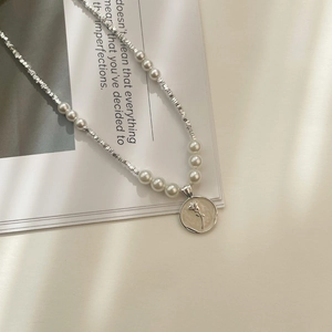Detail of S925 silver beaded pearl necklace with embossed rose pendant on vintage book