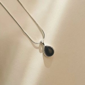 Detail of water drop black agate pendant on sleek silver snake chain with shadows