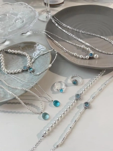 Collection of pearl necklaces and bracelets with light blue gemstones on grey tray