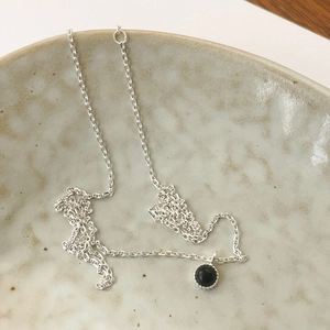 Close-up of S925 silver necklace with black crystal pendant on a ceramic plate