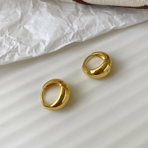Close-up of polished gold-plated drop hoop earrings on a minimalist white textured background