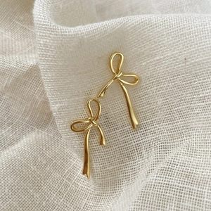 Boucles d'oreilles minimalistes nœud doré avec finition polie sur fond beige texturé