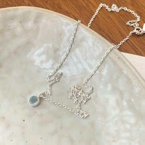Detail of S925 silver necklace with light blue crystal pendant on a ceramic plate
