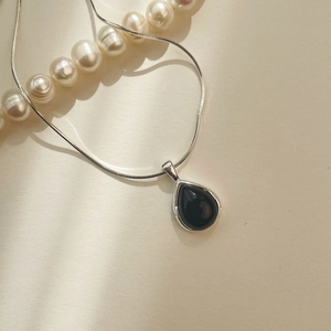 Close-up of black agate teardrop pendant on a sleek silver snake chain with soft shadows