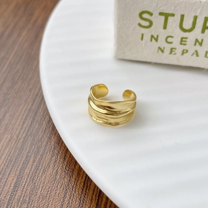 Detailed macro view of gold ear cuff with irregular layered texture on white plate