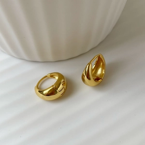 Macro shot of chunky gold drop earrings on a minimalist textured white background
