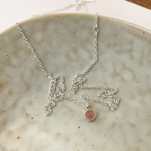 Detail of a round pink crystal pendant with serrated silver edges on a ceramic plate